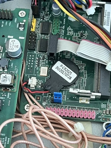 The round battery glued to the motherboard, its red and black leads running to a white connector